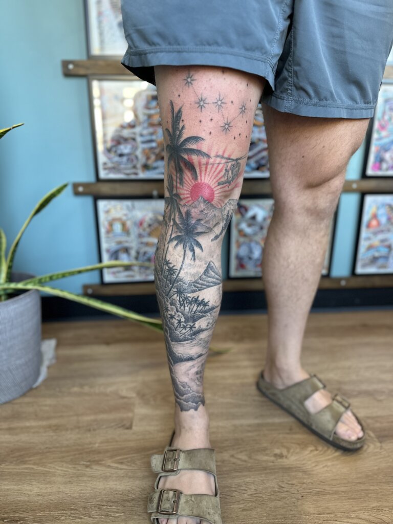mountain and palm tree scene tattoo on leg
